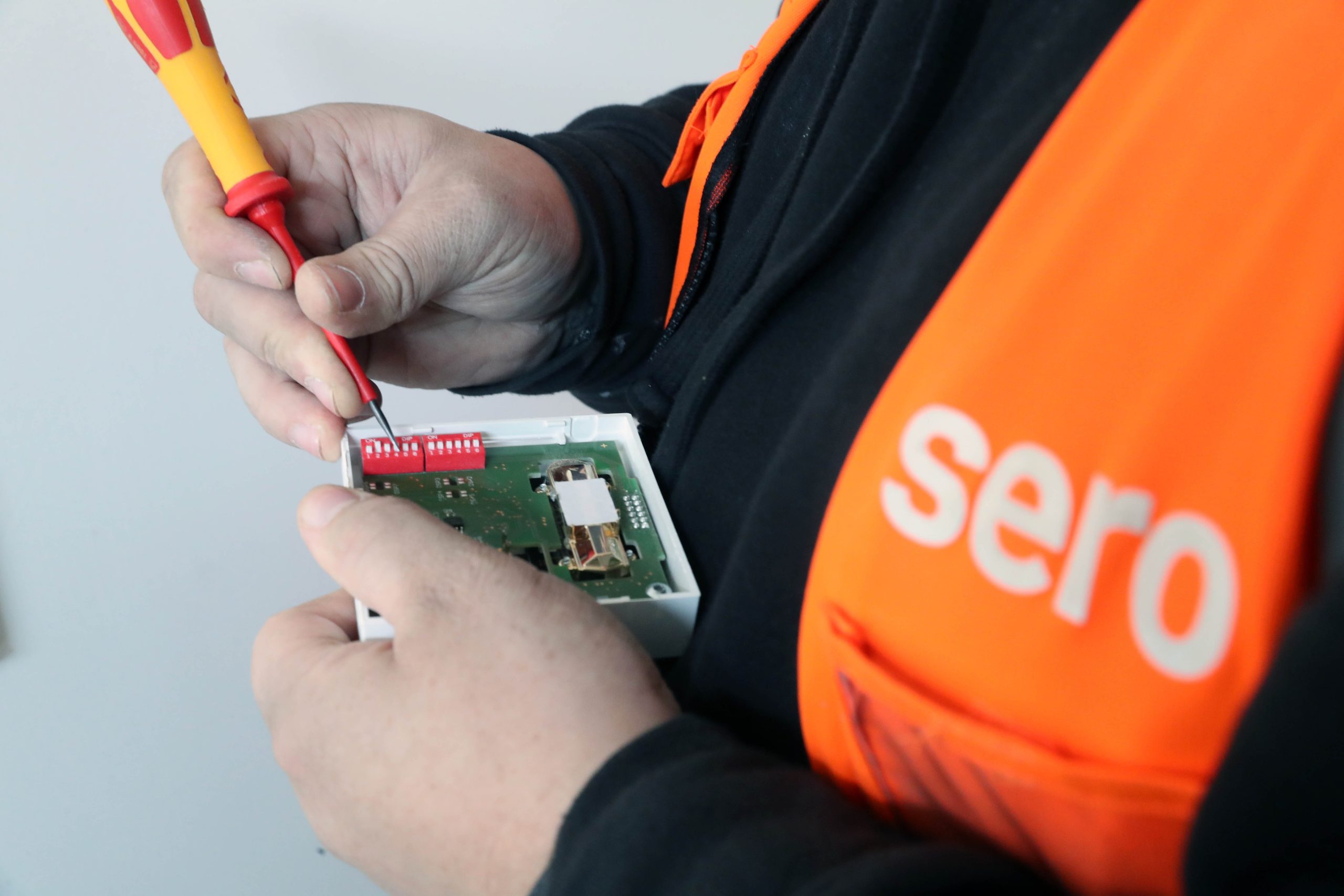 A person wearing an orange vest with Sero logo, fixing a device