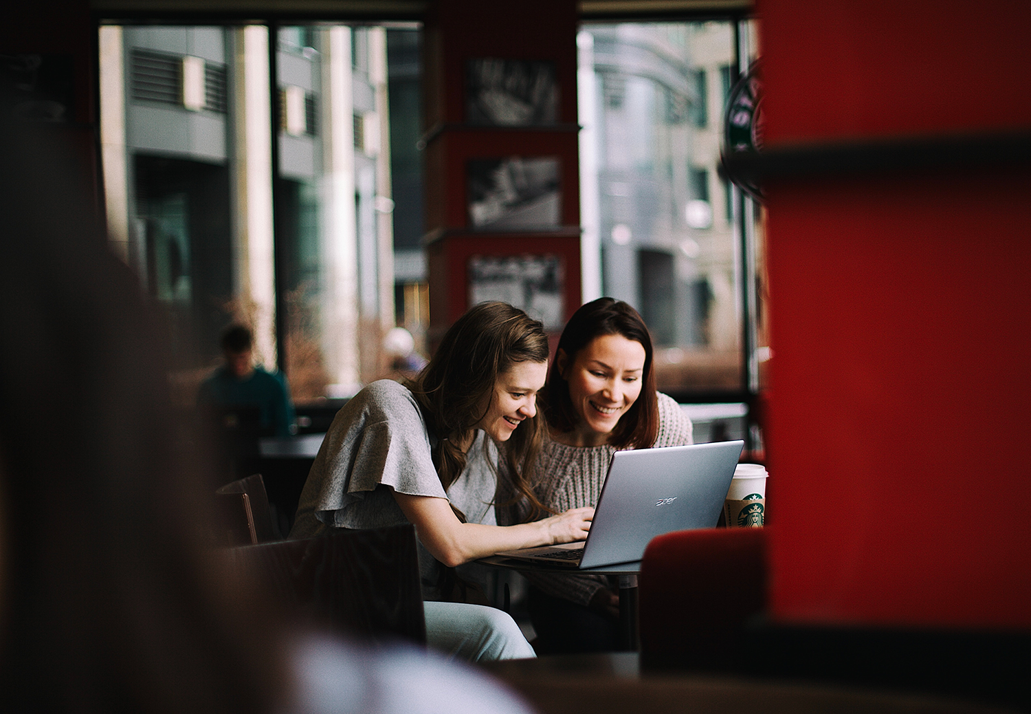 Two young women sat in a coffee shop working on a laptop.
